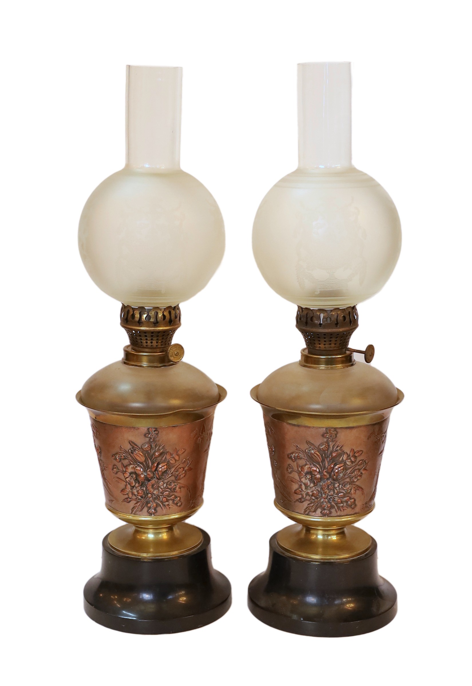 A pair of Victorian copper and brass oil lamps with aesthetic style floral decoration, black marble bases and unusual frosted glass shades with internal flues, height overall 50cm